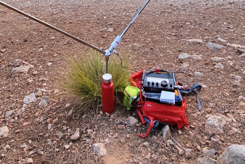 Picture of a portable amateur radio operating station showing antenna, radio, lifepo4 battery, backpack, and water bottle.